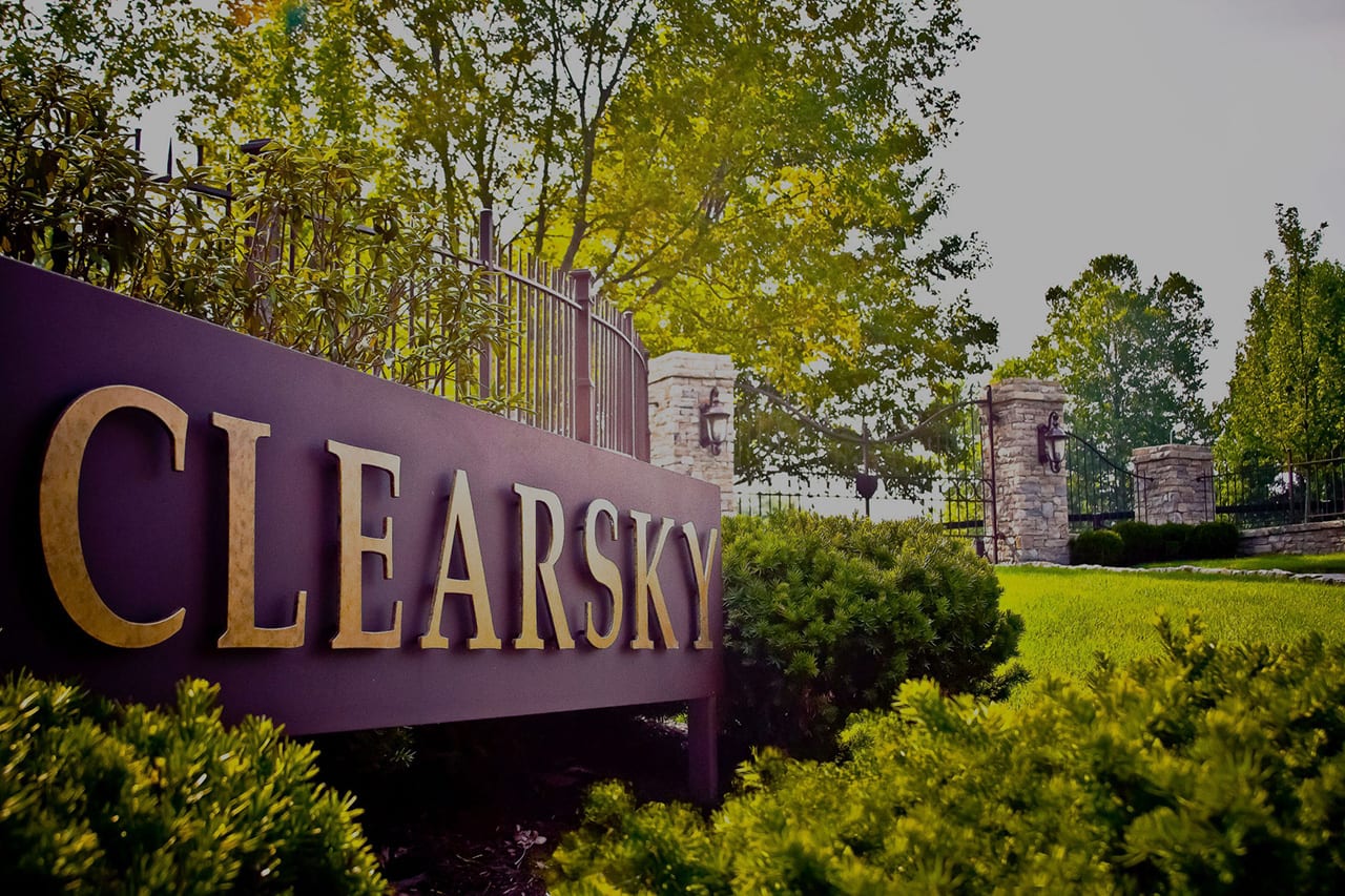 The aubergine Clearsky Farms entrance sign with bronze lettering, set among stone piers and Kentucky greenery